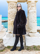 Riviera Noir Black Mink Swing Coat flared open with ocean waves in the background. Statement mink fur coat for luxury winter style.