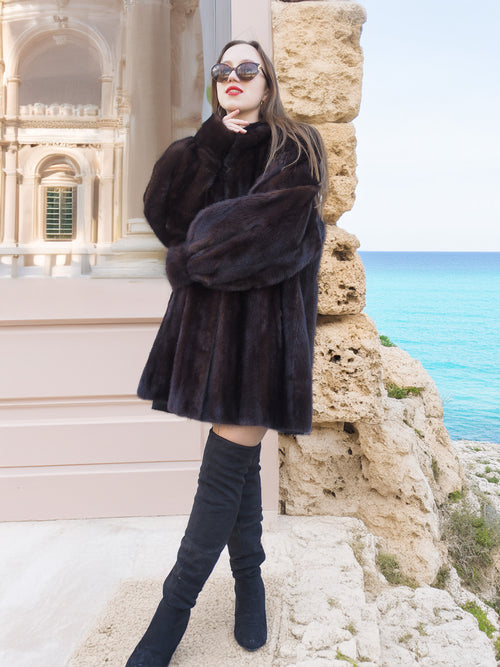 Black Mink Swing Coat - Riviera Noir styled in front of a stone building by the sea. Elegant and warm fur coat for winter fashion.