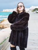 Riviera Noir Black Mink Swing Coat worn on a boardwalk near turquoise waters. Luxurious fur outerwear for sophisticated winter wear.
