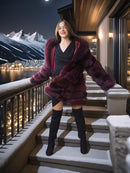 Woman in a fur coat standing on snow-covered steps with a mountainous background