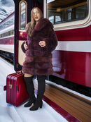 Woman in a fur coat standing next to a vintage train with a red suitcase.