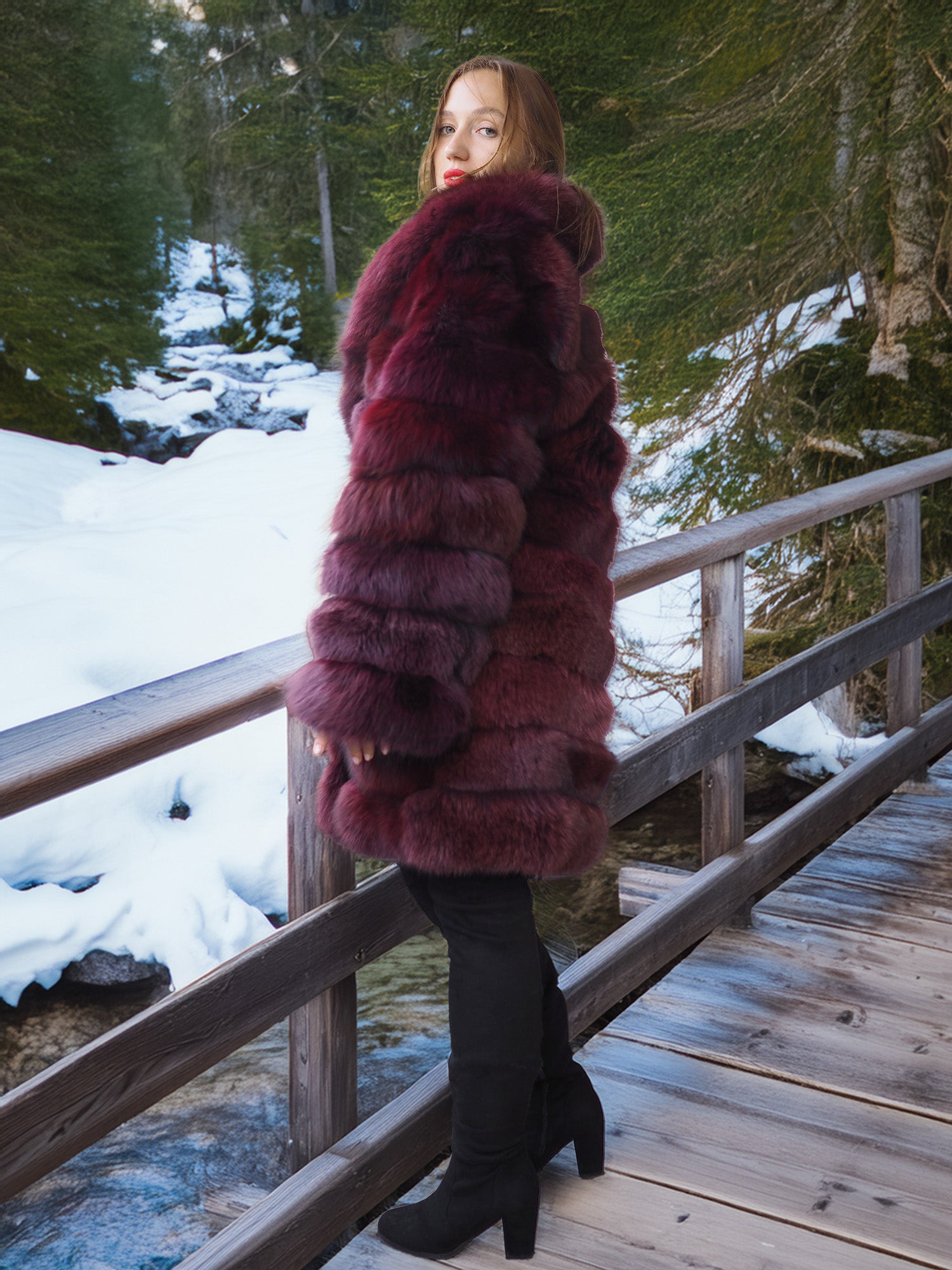 Person wearing a fur coat standing on a wooden bridge with a snowy forest background