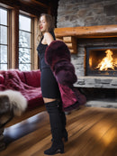 Woman in a black dress with a fur stole standing in front of a fireplace.