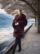 Woman in a fur coat standing by a lake with mountains in the background