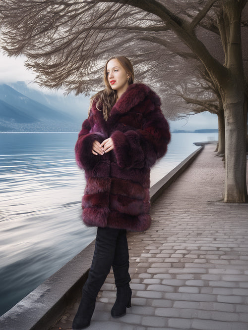 Woman in a fur coat standing by a lake with mountains in the background