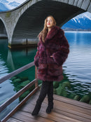 Woman in a fur coat standing on a wooden platform by a lake with mountains in the background