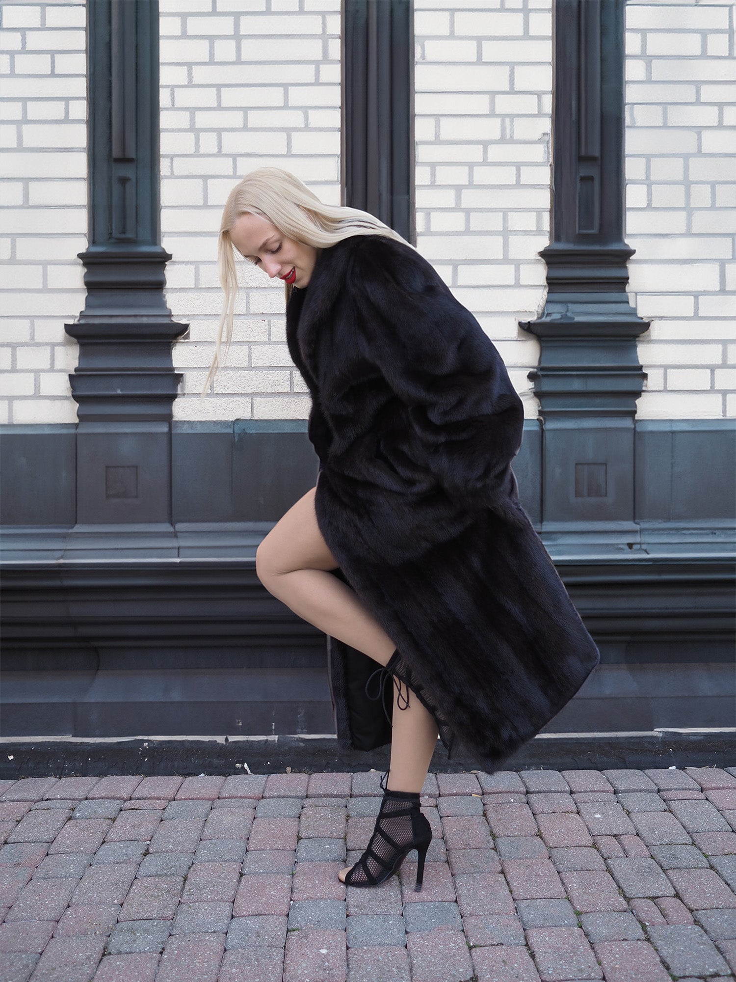 Luxurious black mink fur coat on stylish woman posing near brick building