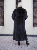 Luxurious black mink fur coat, featuring full-length styling and a plush, high-quality appearance, showcased against a modern architectural backdrop.