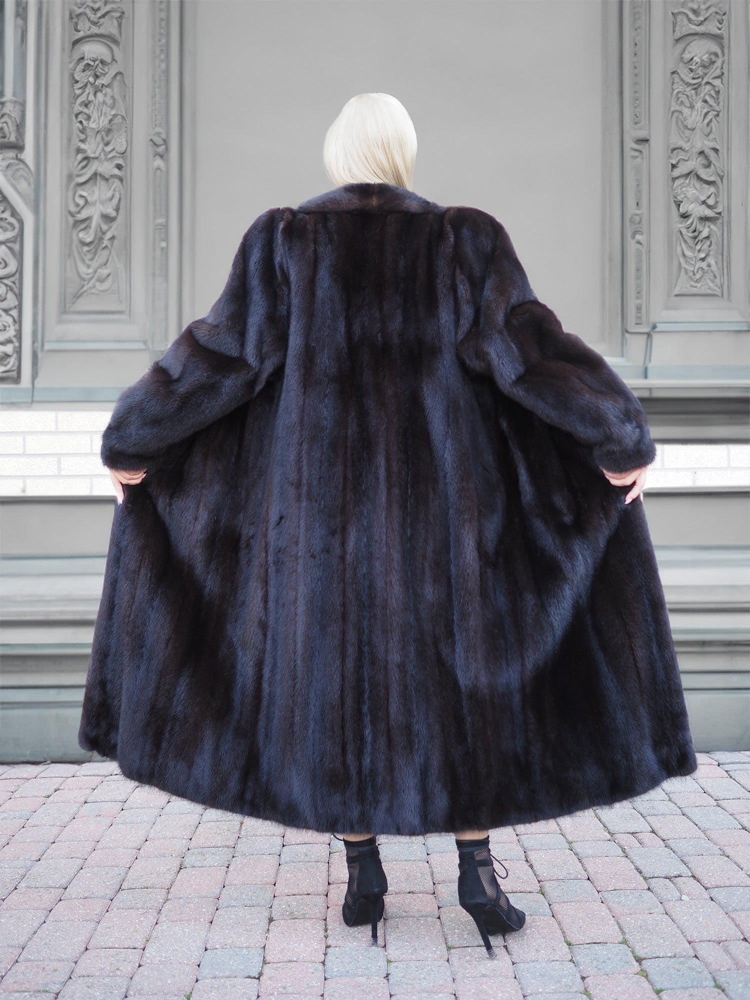 Luxurious black mink fur coat with elegant design and tailored fit, showcased against an ornate architectural background.
