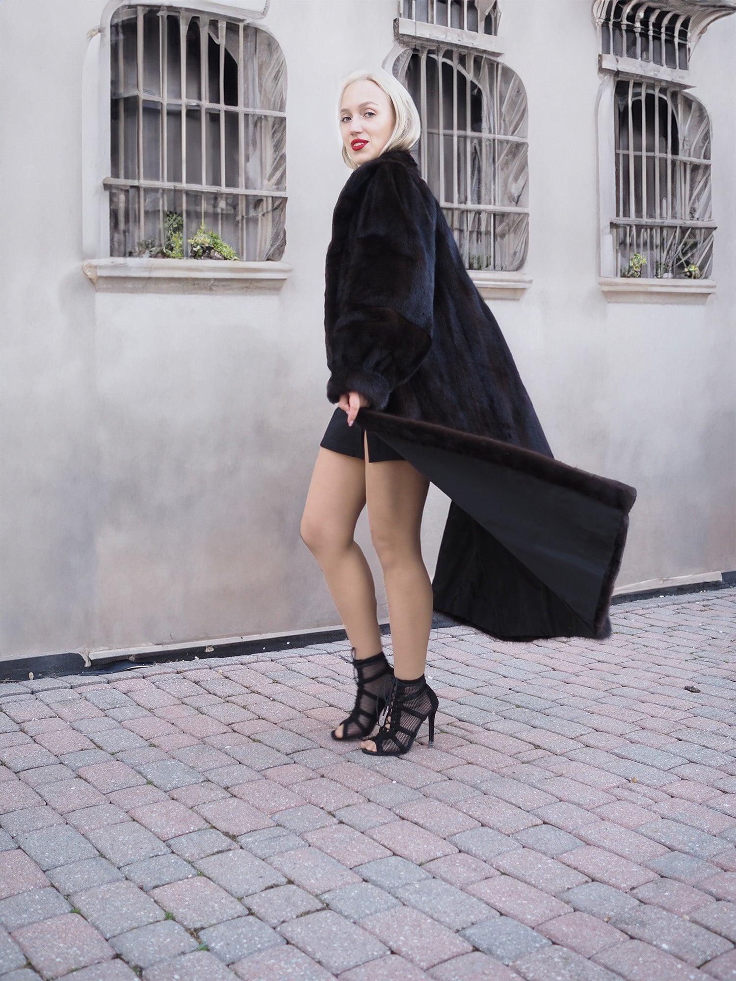 Black faux fur coat and high heels, fashionable woman posing on brick pavement