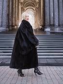 Luxurious black mink fur coat, elegant woman stands on steps of grand building