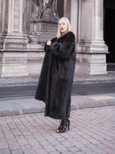 Elegant woman in long black fur coat standing near historic building
