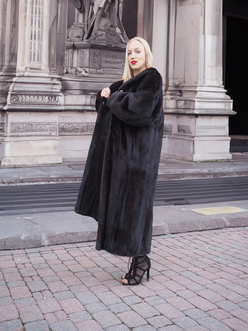 Elegant woman in long black fur coat standing near historic building