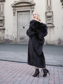 Elegant black mink fur coat with flared silhouette, worn by a stylish woman in front of a historic building.
