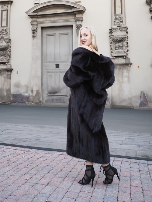 Elegant black mink fur coat with flared silhouette, worn by a stylish woman in front of a historic building.