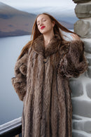 Woman wearing a fur coat standing by a stone wall with a scenic background