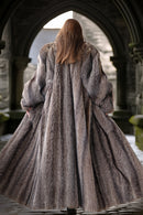 Person wearing a long fur coat standing in an archway.