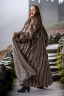 Woman wearing a fur coat standing on a path with a natural landscape background