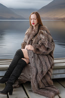 Woman in a fur coat sitting on a dock with a scenic background
