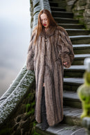 Woman in a fur coat standing on stone steps with a snowy landscape.