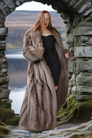 Woman in a fur coat standing in a stone archway with a scenic background