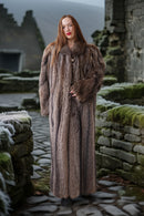 Woman in a fur coat standing in stone ruins with a misty landscape.