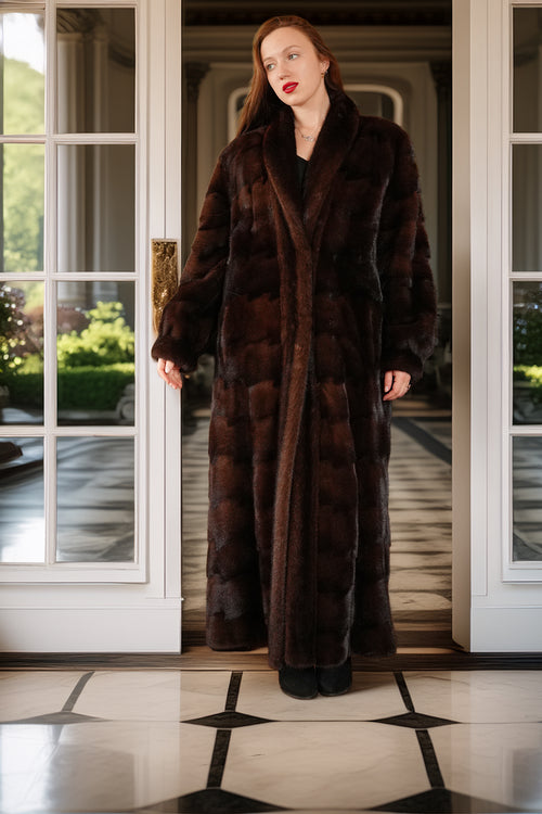 Woman wearing a long brown fur coat standing in a doorway.
