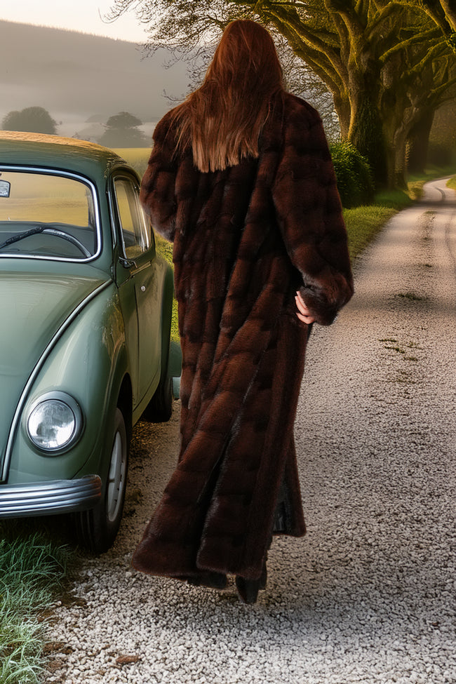 Person in a long brown fur coat walking away from a vintage car on a road.