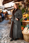 Woman in a long dark coat with fur trim standing in an outdoor market setting.