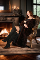 Woman sitting in a chair by a fireplace wearing a fur coat and black boots.