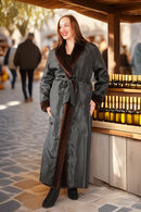 Woman in a long gray coat with fur trim standing in an outdoor setting.