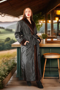 Woman in a long dark coat with fur trim standing in a rustic outdoor setting.