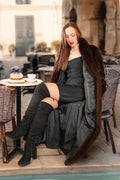 Woman in a black dress and fur coat sitting at an outdoor cafe table.