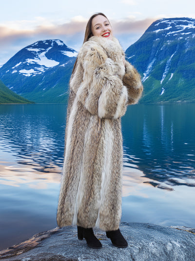 Full-length Coyote Fur Coat in natural tones, styled for warmth and elegance beside a reflective mountain lake.