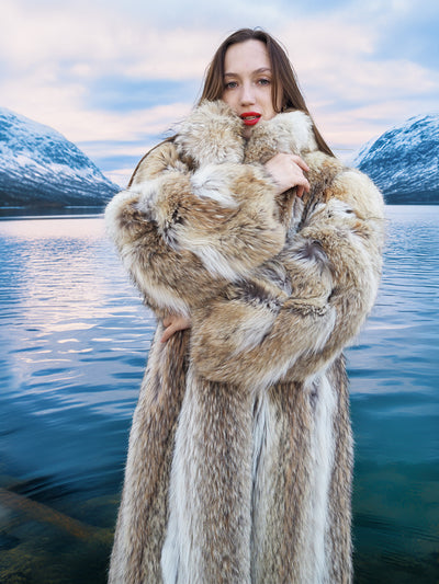 Model wrapped in thick Coyote Fur Coat, showcasing luxurious texture and warmth by a snowy alpine lake.
