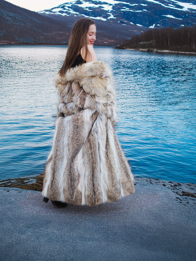 Back view of full-length Coyote Fur Coat, showcasing natural fur texture and volume beside a mountain lake.