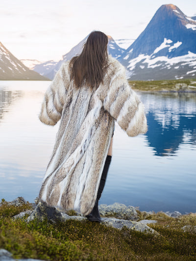 Back view of flowing Vintage Coyote Fur Coat, highlighting natural fur stripes in a serene mountain landscape.