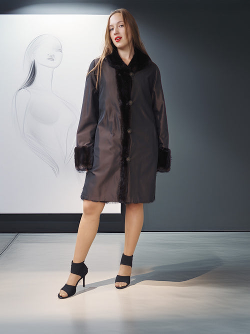 Woman wearing a dark coat with fur trim standing in front of a whiteboard with a design on it.