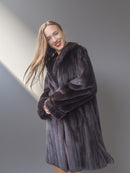 Woman wearing a dark fur coat against a plain background