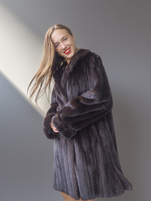 Woman wearing a dark fur coat against a plain background