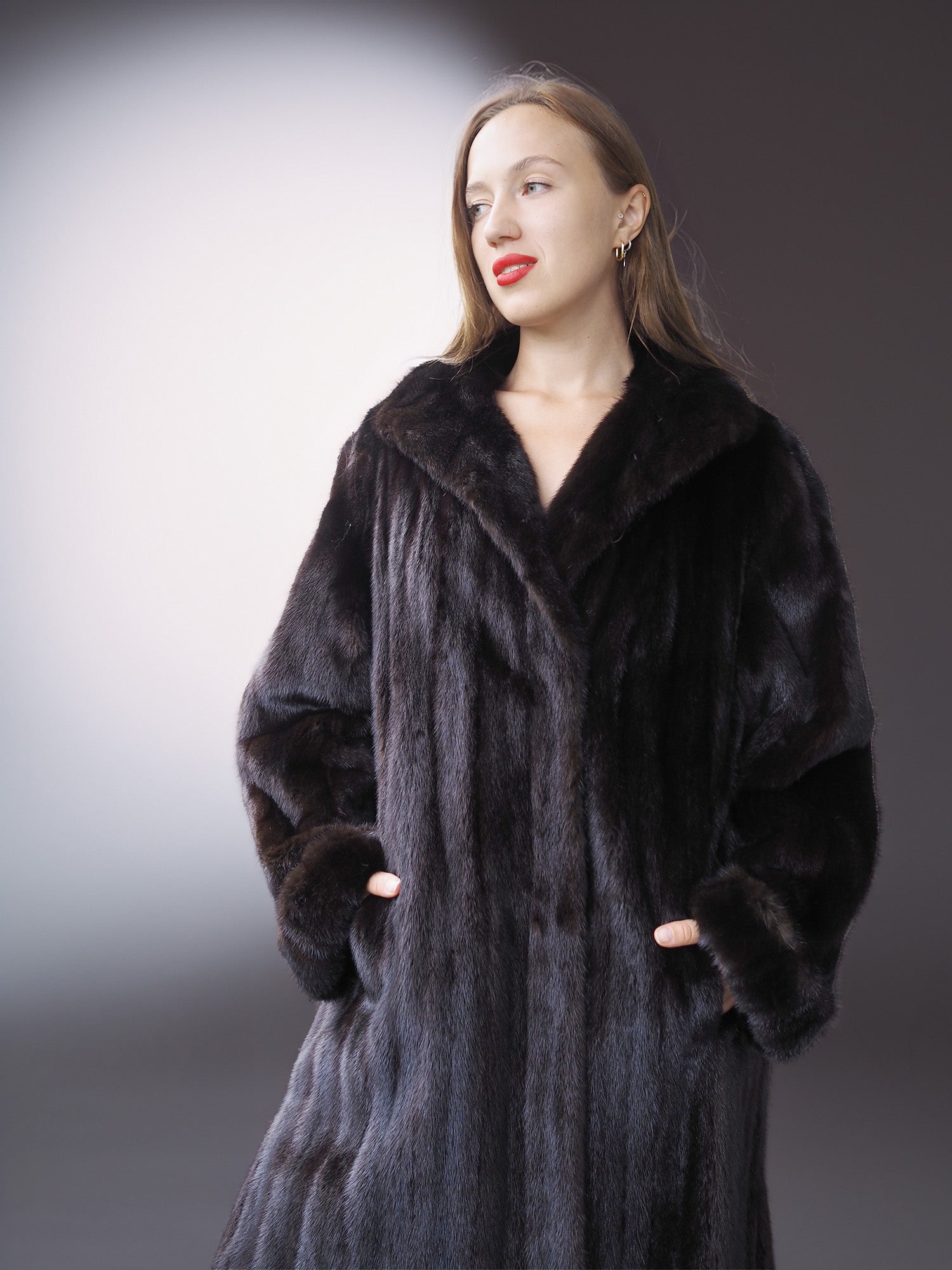 Woman wearing a long black fur coat against a gradient background