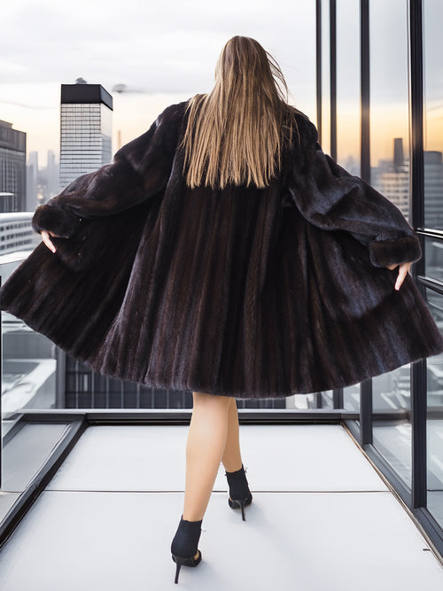 Person wearing a dark fur coat standing in front of a cityscape with tall buildings.