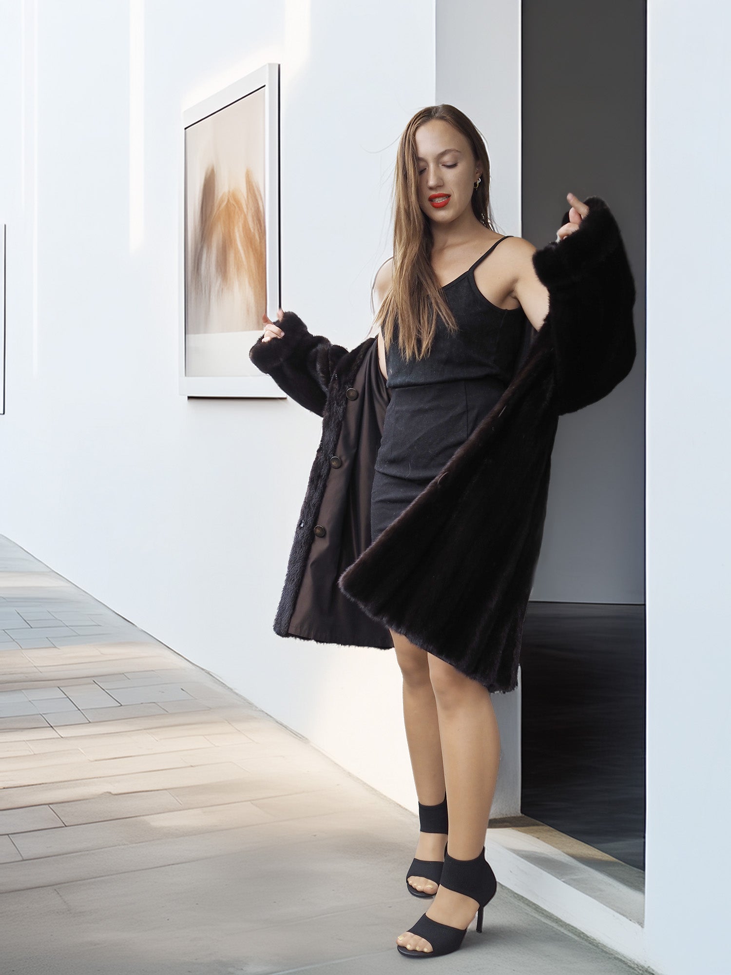 Woman in a black dress and coat standing in a modern interior setting.