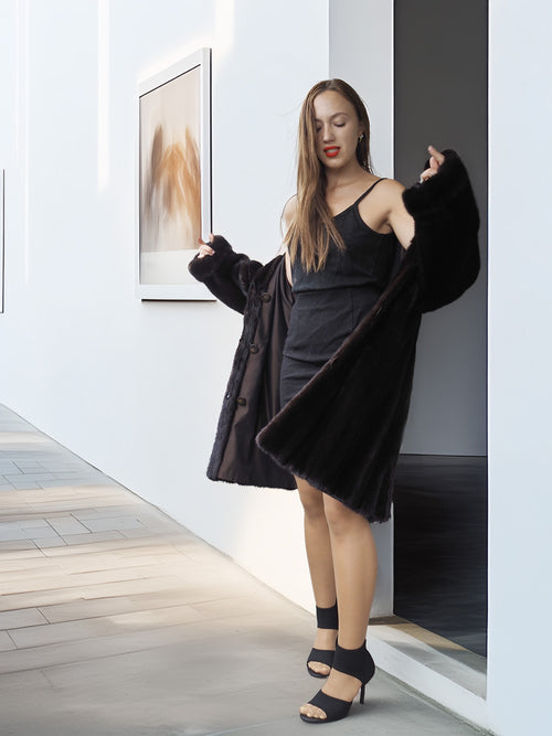Woman in a black dress and coat standing in a modern interior setting.