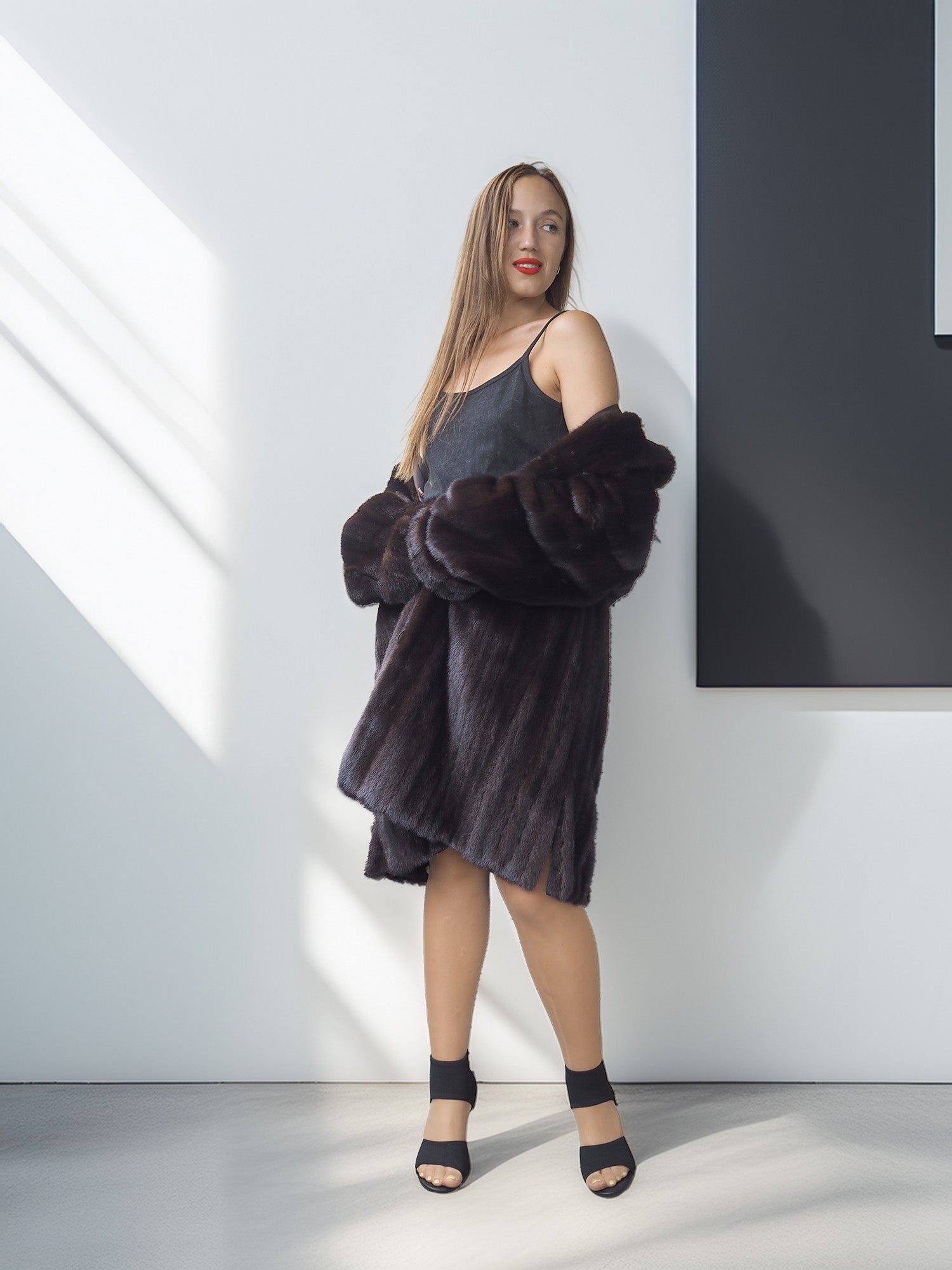 Woman wearing a dark fur coat over a gray dress in a minimalistic setting