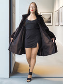 Woman wearing a black coat and dress standing indoors.