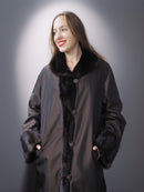 Woman wearing a long dark coat with fur trim against a gray background