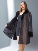 Woman wearing a black coat with fur trim against a gray background