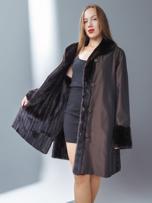 Woman wearing a black coat with fur trim against a gray background