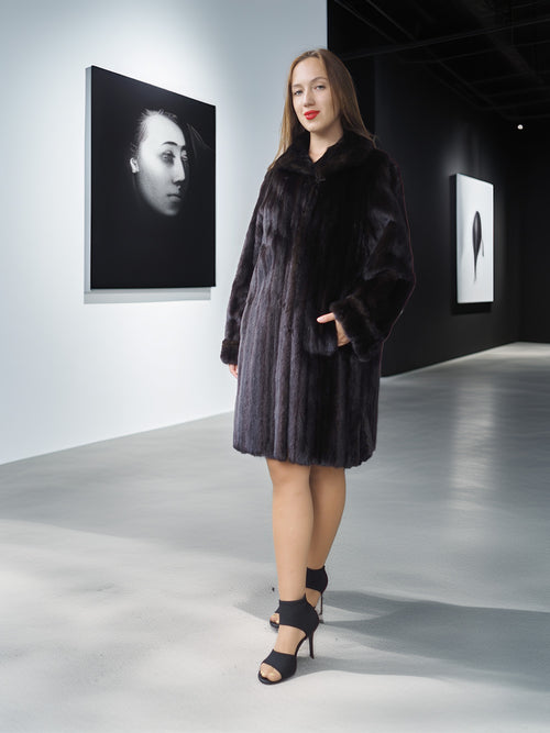 Woman in a black fur coat standing in an art gallery with artworks on the walls.